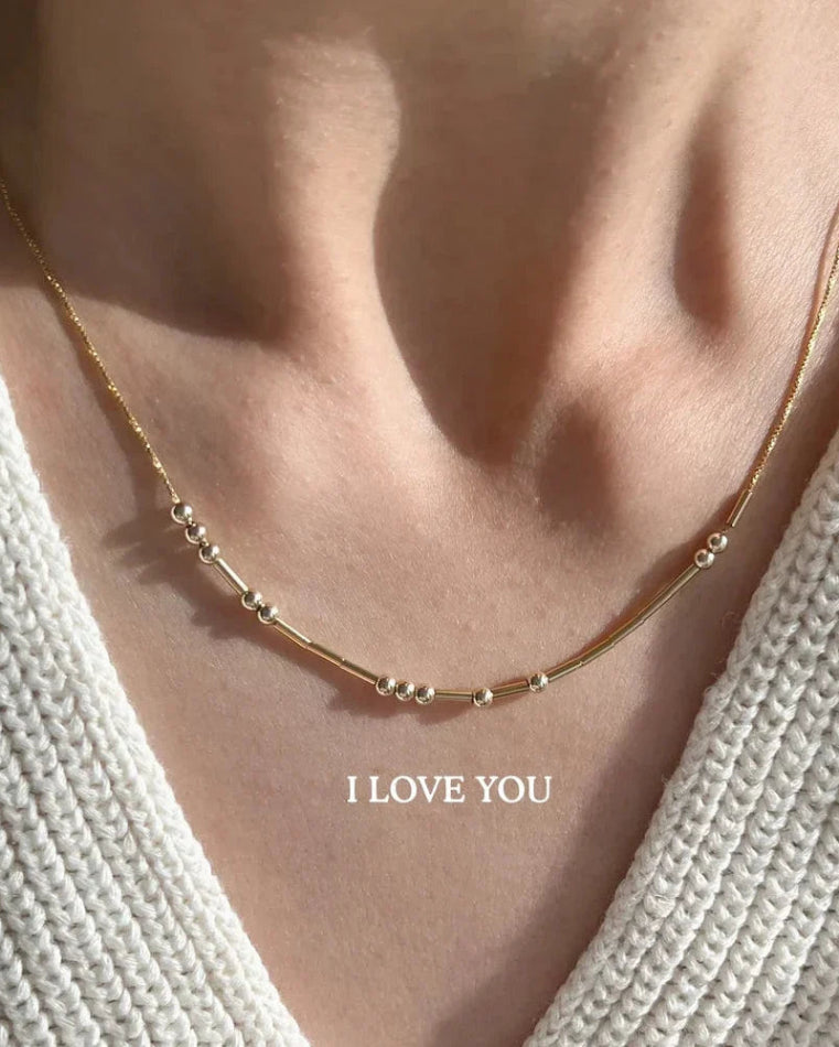 Gold necklace with small beads on a person wearing a white textured garment, with 'I LOVE YOU' Morse Code